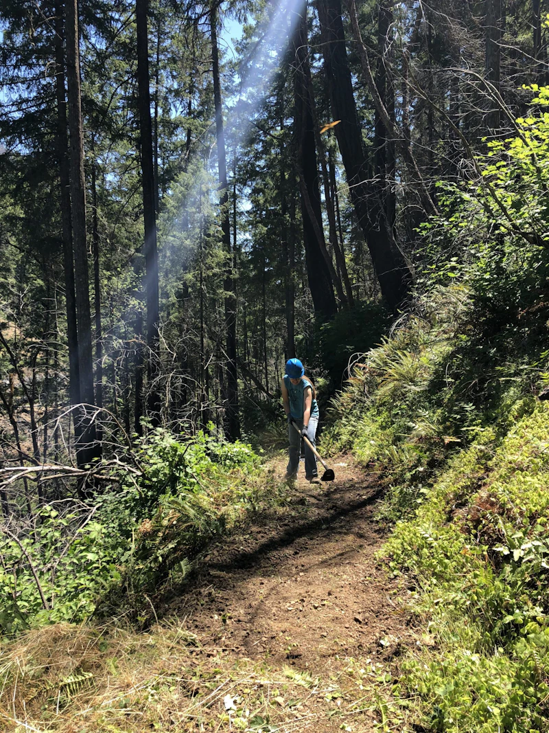 volunteer with hoe on a dirt trail in the forest