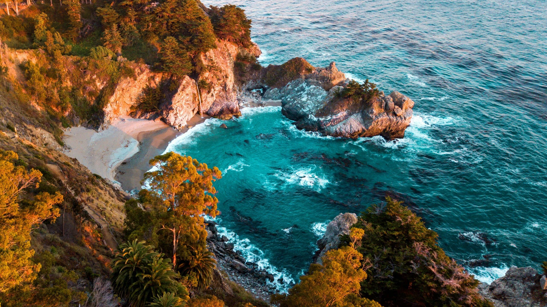 Sandy beach surrounded by rocky cliffs at sunset.