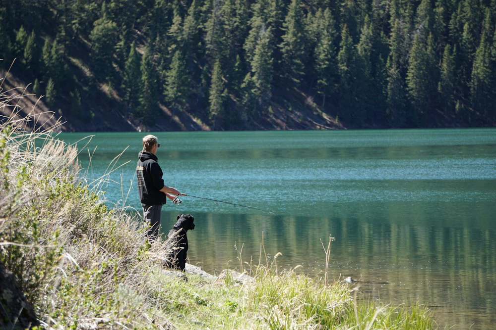 a man and his dog fishes on the shore of a lake