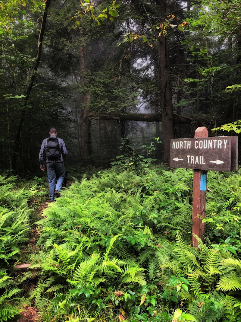 a man walking down a narrow trail in front of a trail sign