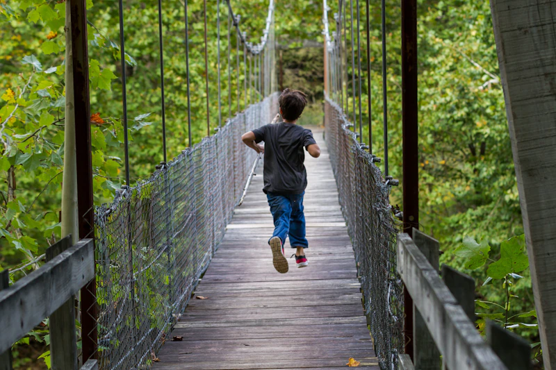 Young boy runs across a trail bridge.