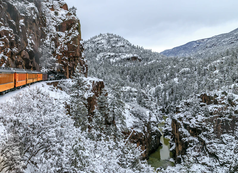 Passenger train rolls through a snowy mountain side.