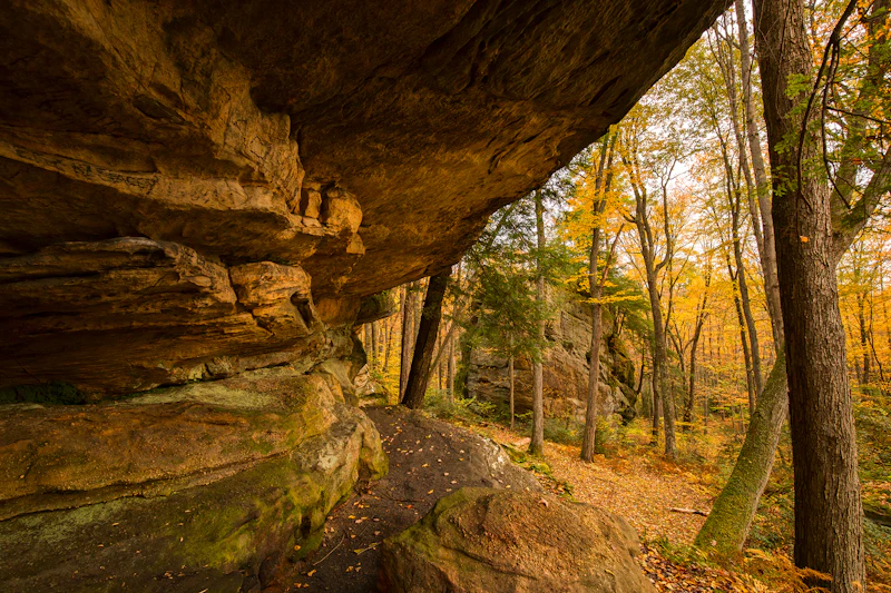 a rock overhang in a forest with fall colors