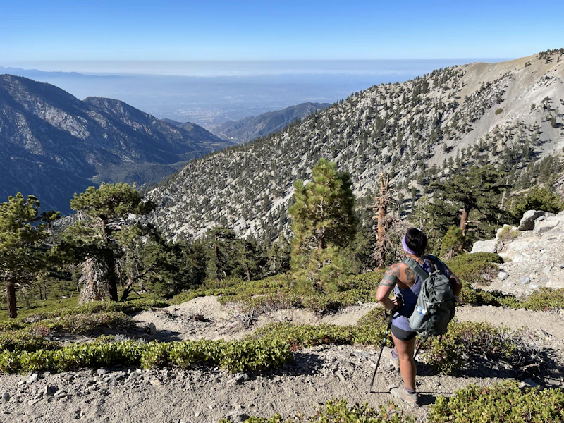 a woman hiking with a backpack overlooks a mountain valley