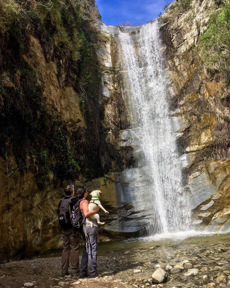 two hikers at the base of a cascading waterfall