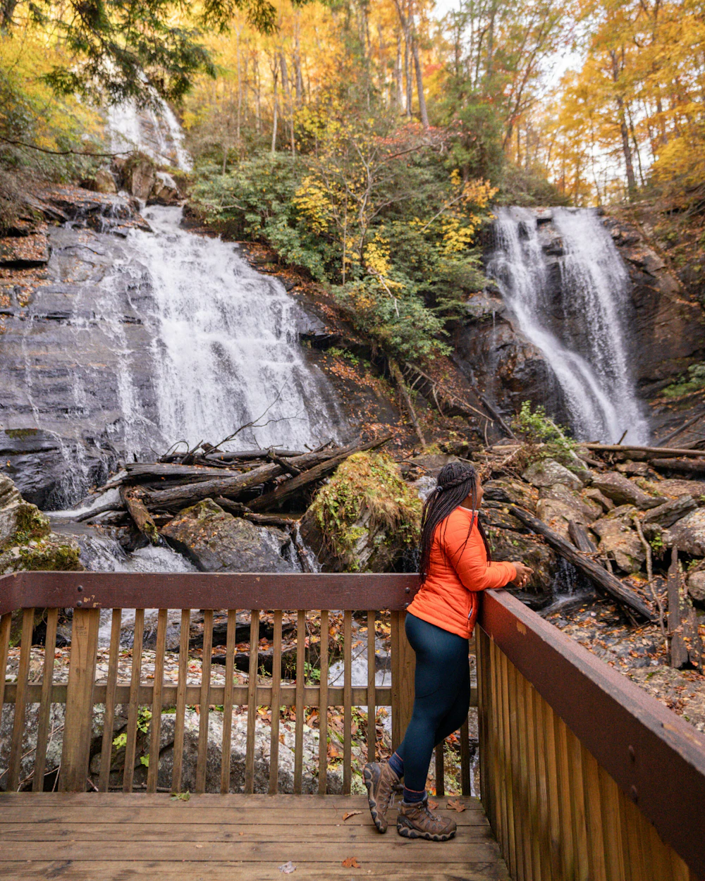 woman standing on a platform viewing waterfall in the forest in fall