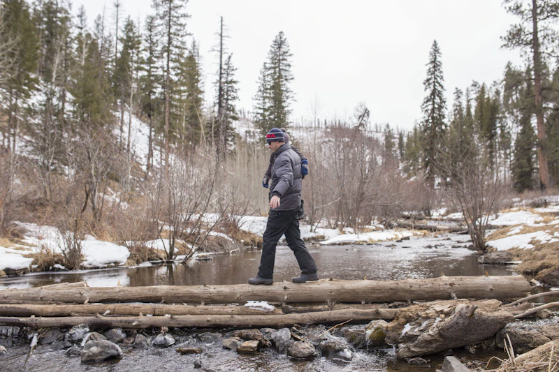 a hiker walking over a log in the winter in a creek