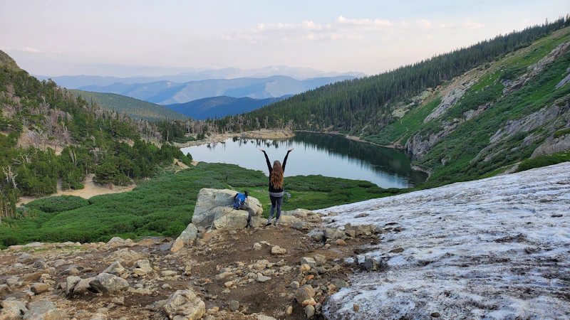 woman with arms raised above an alpine lake