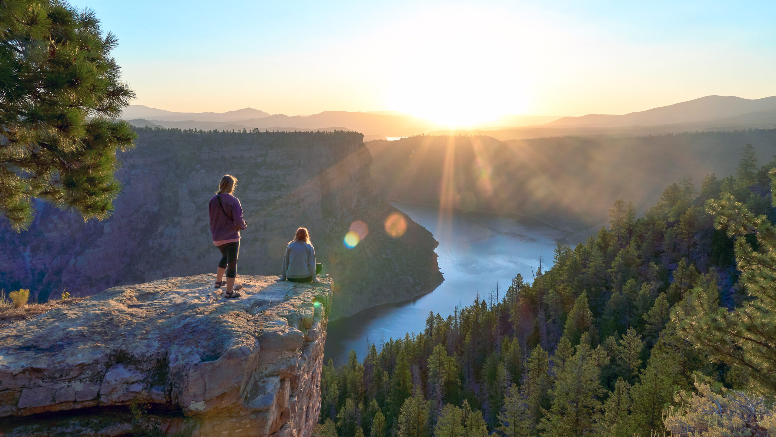 two people sit on a rocky overlook above a water reservoir at sunset