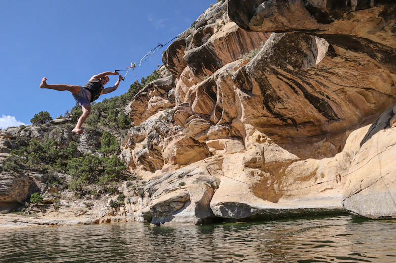 a man swinging off a rope swing into water beneath cliffs