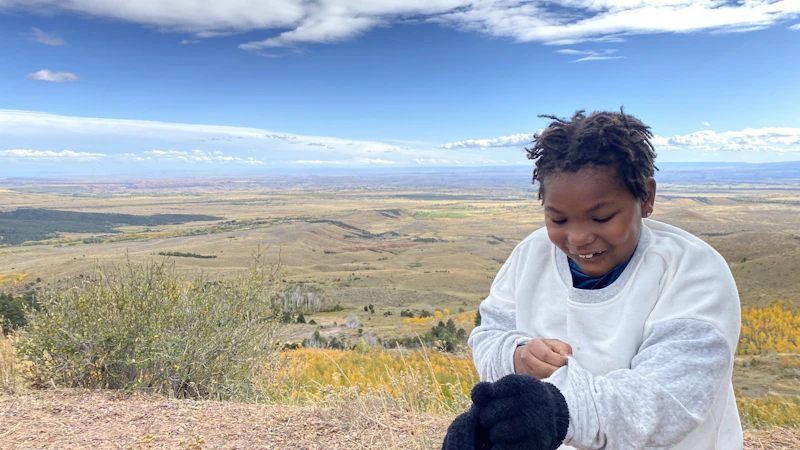 A young person looking at their shirt in front of a vast view behind them