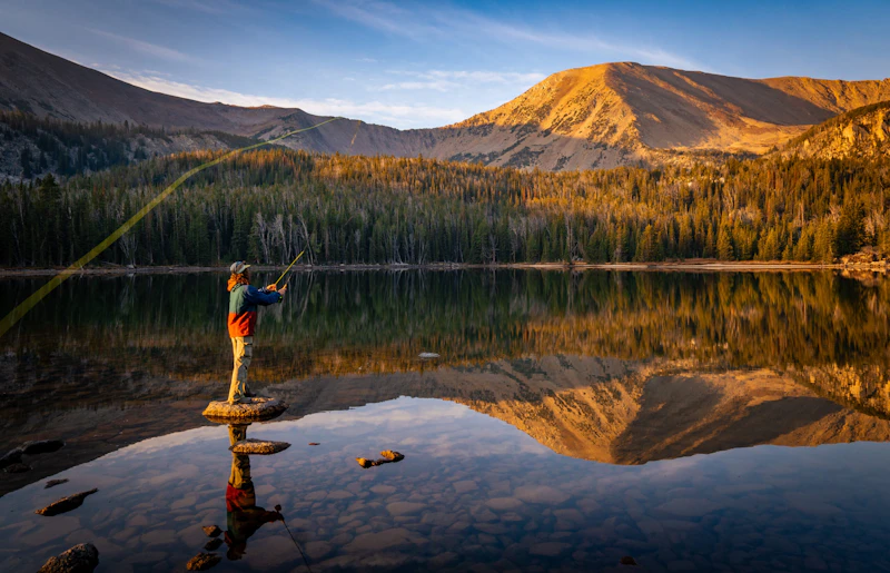 a man stands on a rock and fly fishes in a lake
