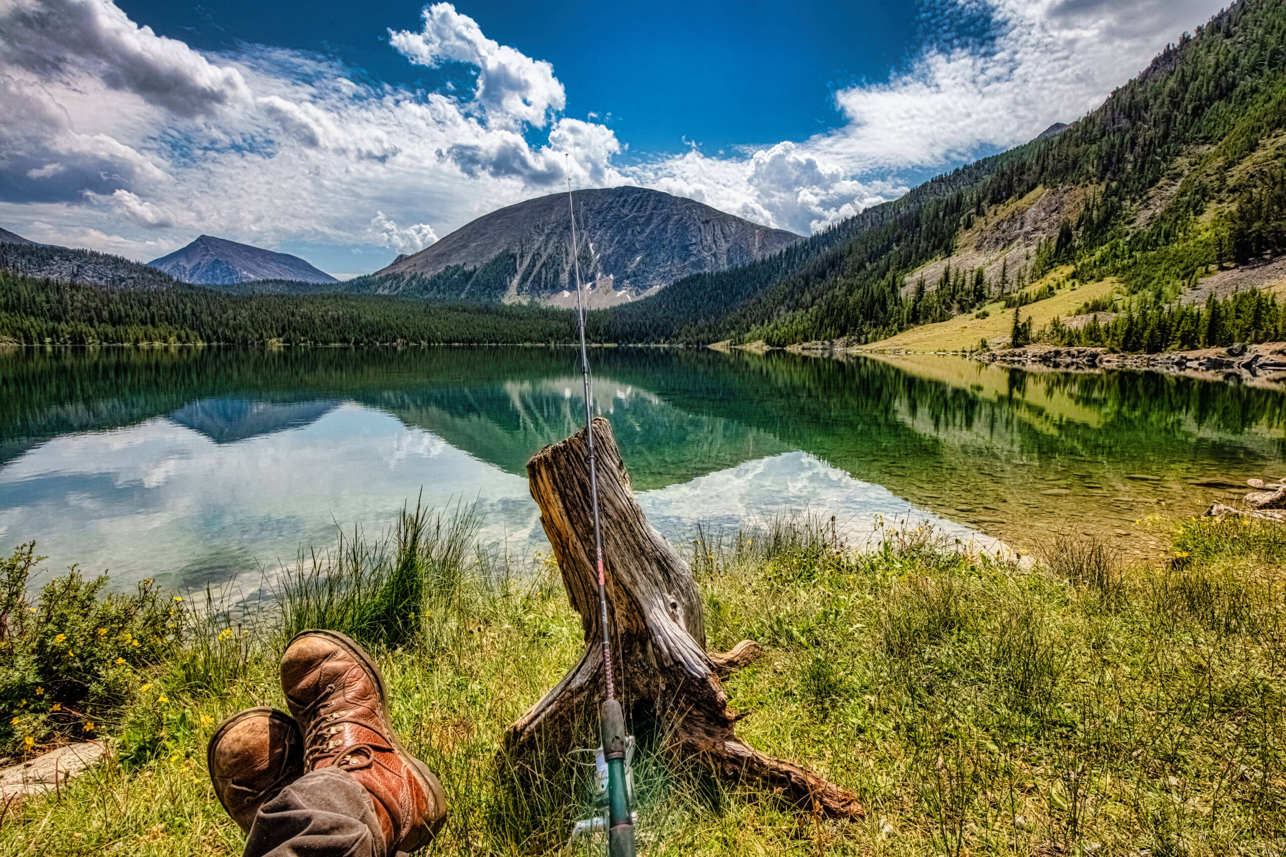 the feet and fishing pole in front of the camera in front of a mountain lake