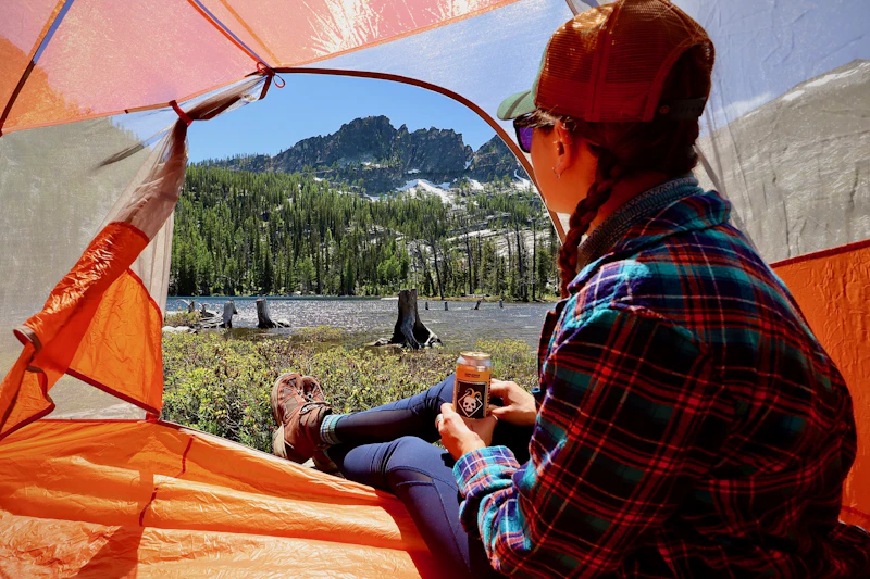 a woman looks out her orange tent to an alpine lake