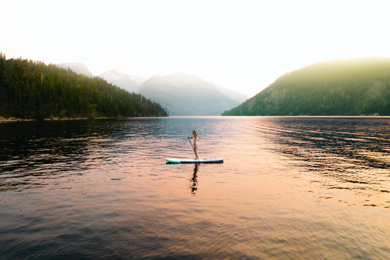 a woman stands on a paddleboard in a calm mountain lake