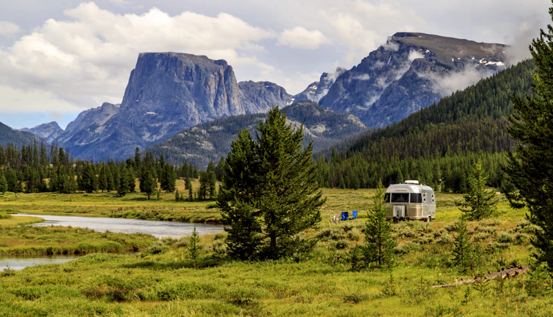 Airstream RV parked by a river with a sweeping mountain view.