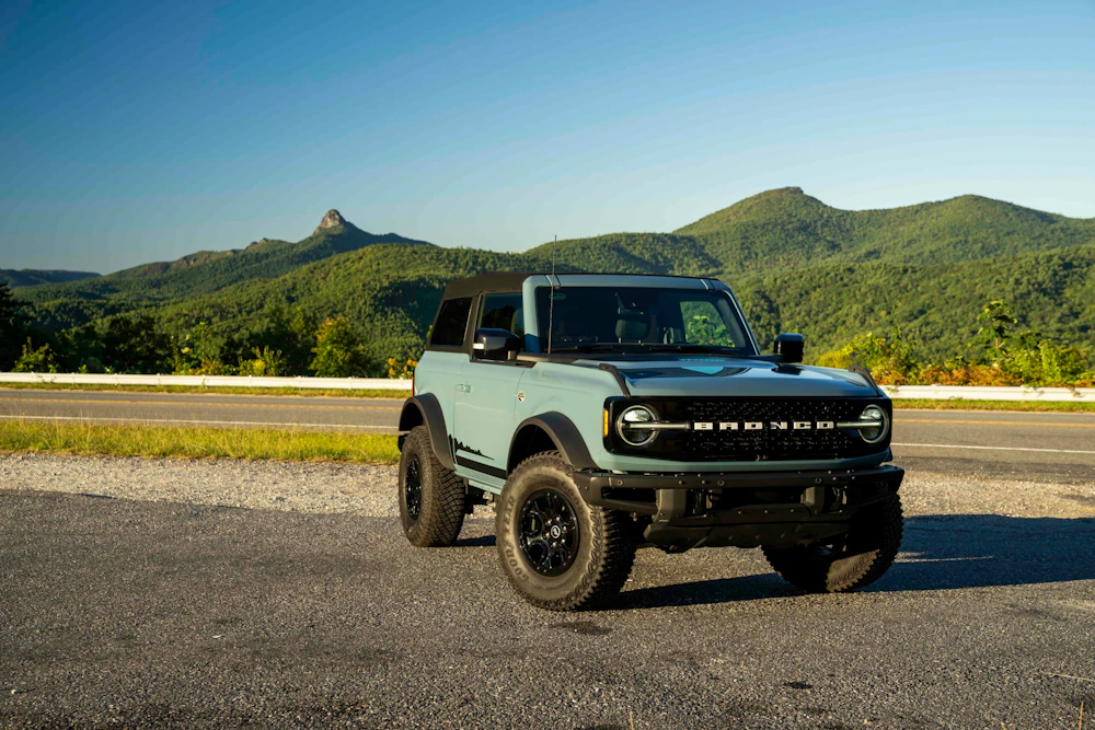 vehicle parked on the side of a road in front of forested mountains