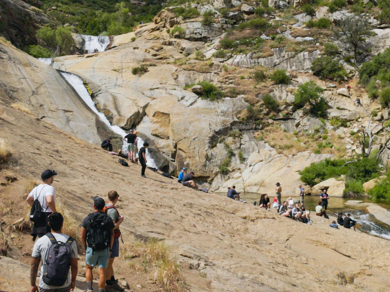 numerous people sit or stand on a rock face near a waterfall