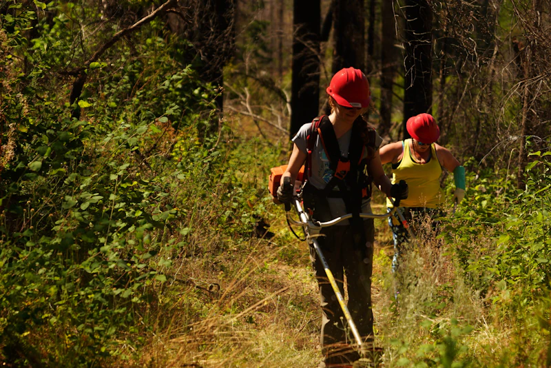 volunteer in hard hat working with a weed wacker in the forest