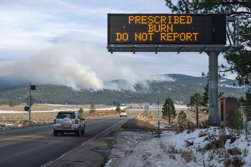 Road sign that reads 'Prescribed burn do not report' with smoke in the distance.