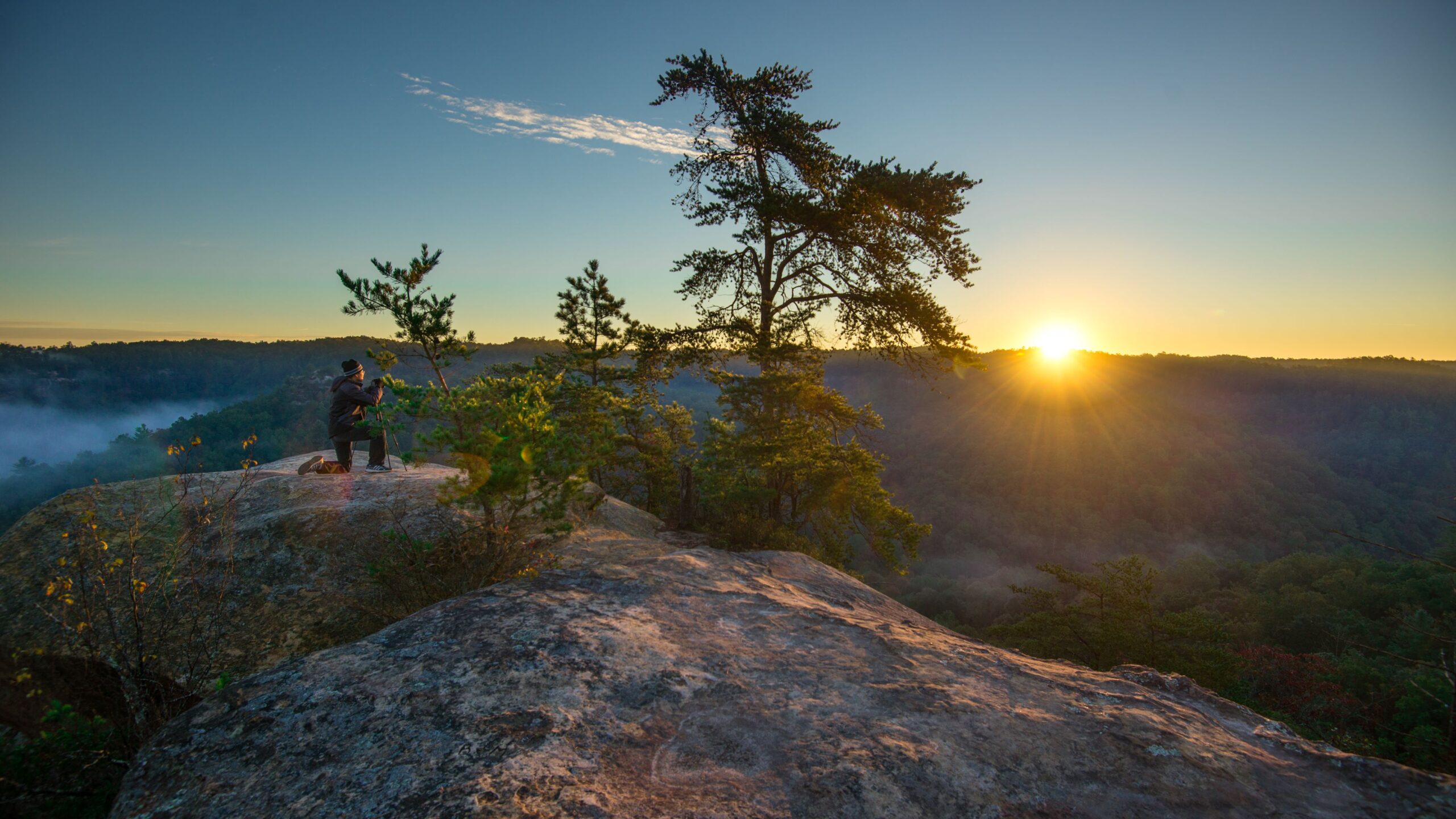 Photographer capturing the sunrise atop a cliff.