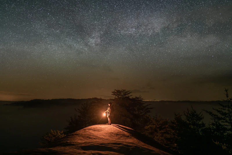 Camper holds a lantern looking up into the end sky.