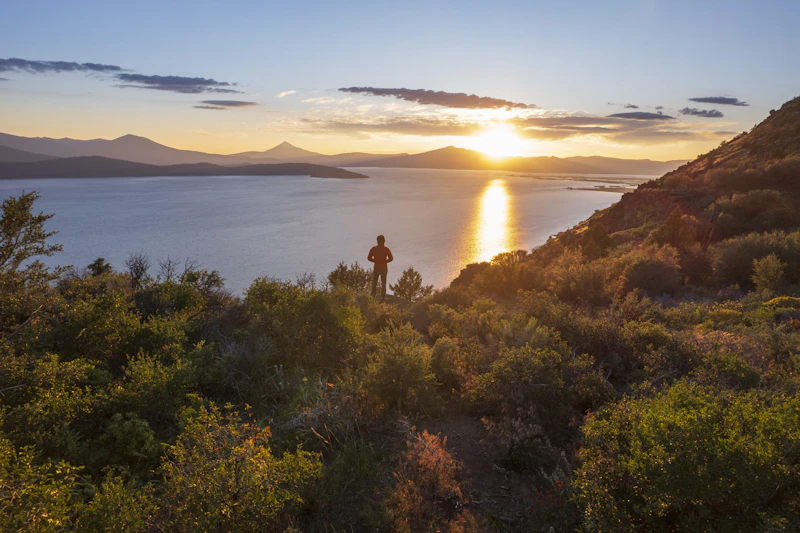 Hiker views a lake from a mountain ridge.