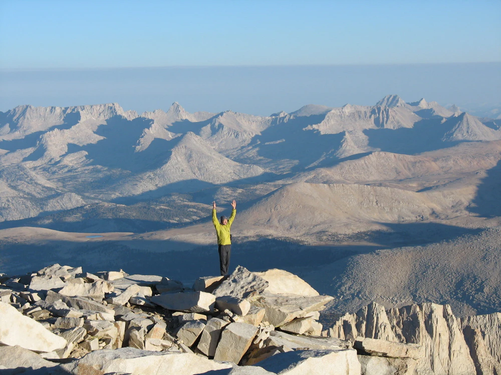 person with arms raised atop a mountain peak