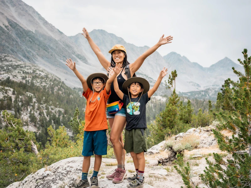 a mom and two sons with their arms up on a hike in a mountain valley