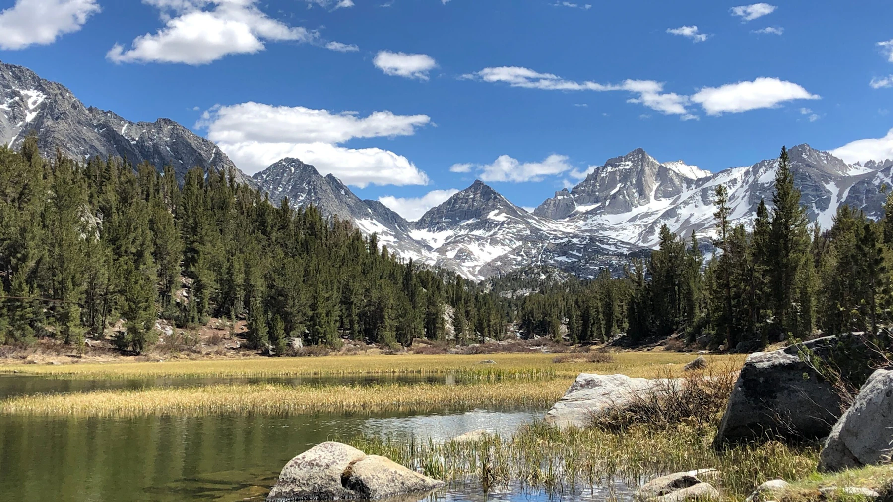 a wide creek flows down from sharp mountain peaks beneath blue skies