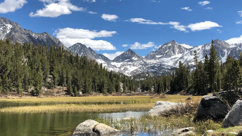 a wide creek flows down from sharp mountain peaks beneath blue skies