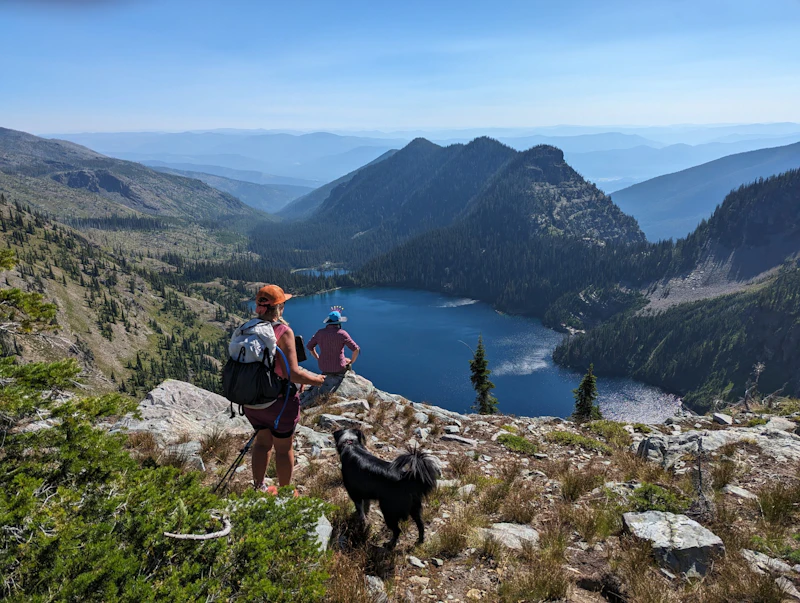 Hikers view a lake from a mountain ridge.
