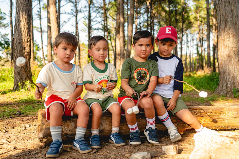 Four brothers sit on a log making s'mores.