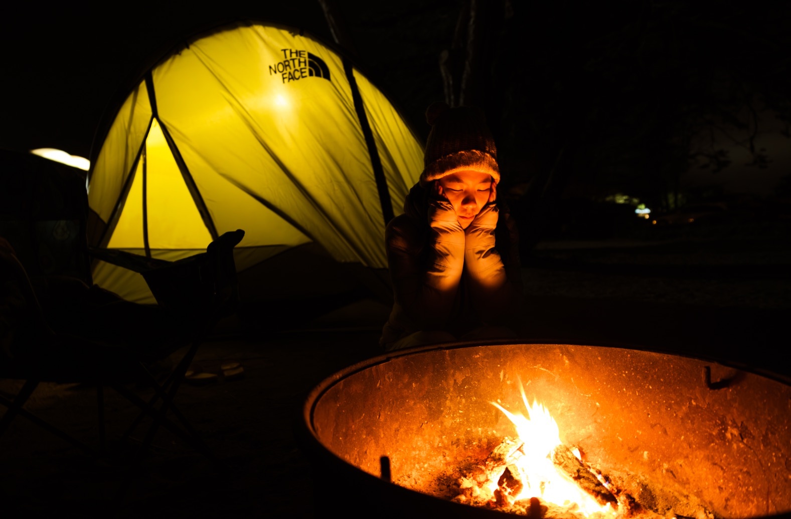 Younge girl sits by the campfire.