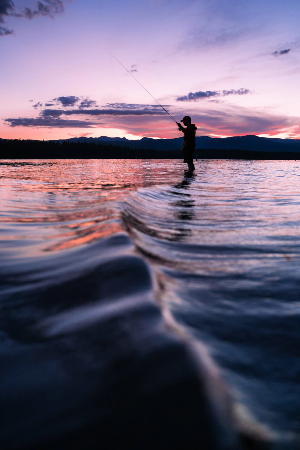 a person stands in shallow water at sunset fly fishing