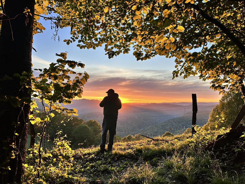 Man stands against a fence watching the sunset over the Appalachians.