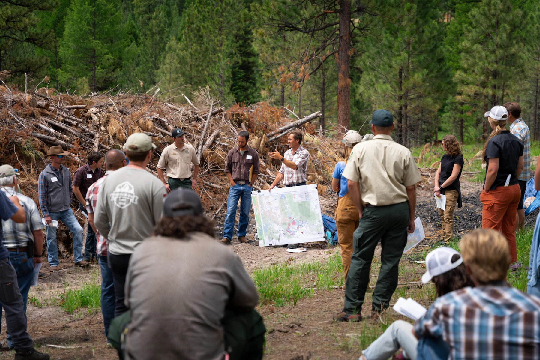 Forest Service staff and partners gather at a project site near Gold Creek for a collaborative planning session, reviewing maps and discussing restoration priorities surrounded by treated timber.