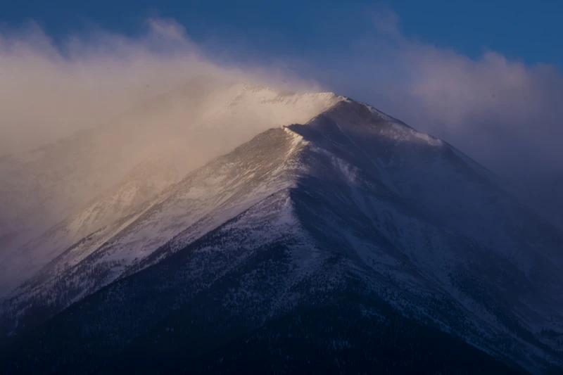 Cloudy drift away from snowy mountain peaks.