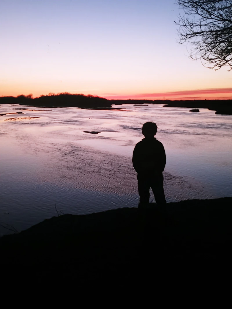Child watches the sunset from the shoreline of a lake.