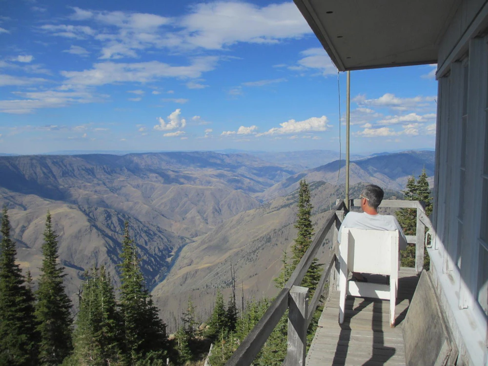 a person sits on the porch of a lookout tower above a canyon