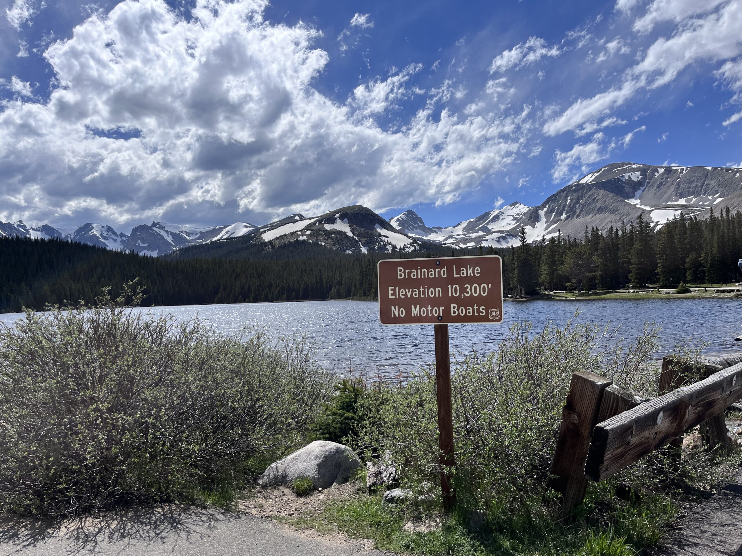 small sign in front of alpine lake and large mountains
