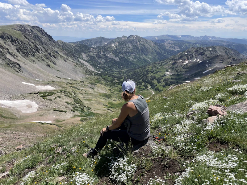 Woman sits in wildflowers, admiring the alpine view.