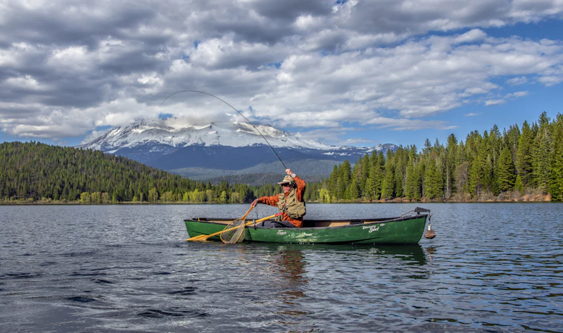 Fisherman boating in a lake framed by Mount Shasta in the distance.
