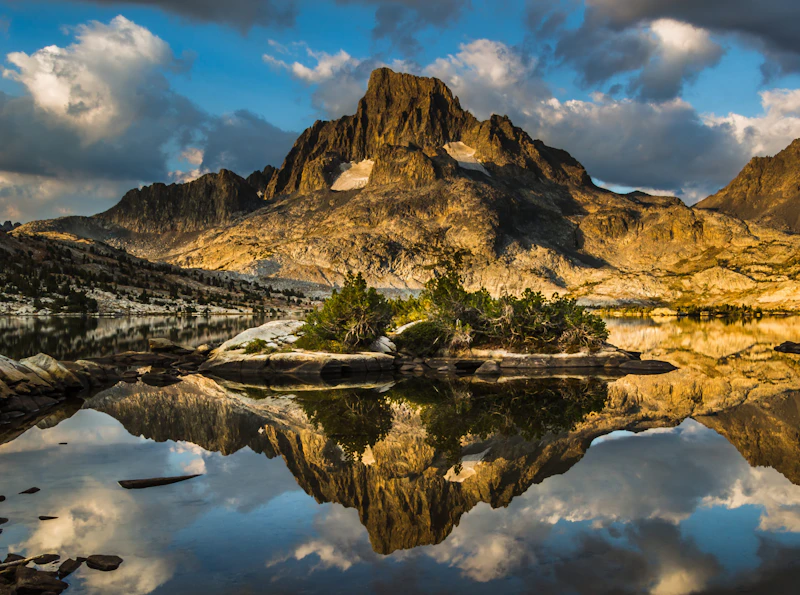 a lone mountain peak reflects info an alpine lake at sunset