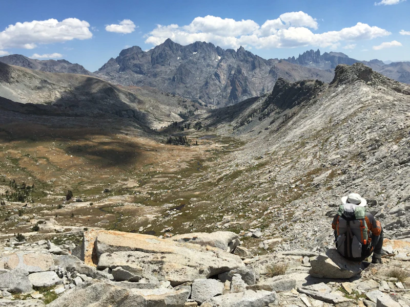 a hiker sits and takes in a vast mountain valley and view