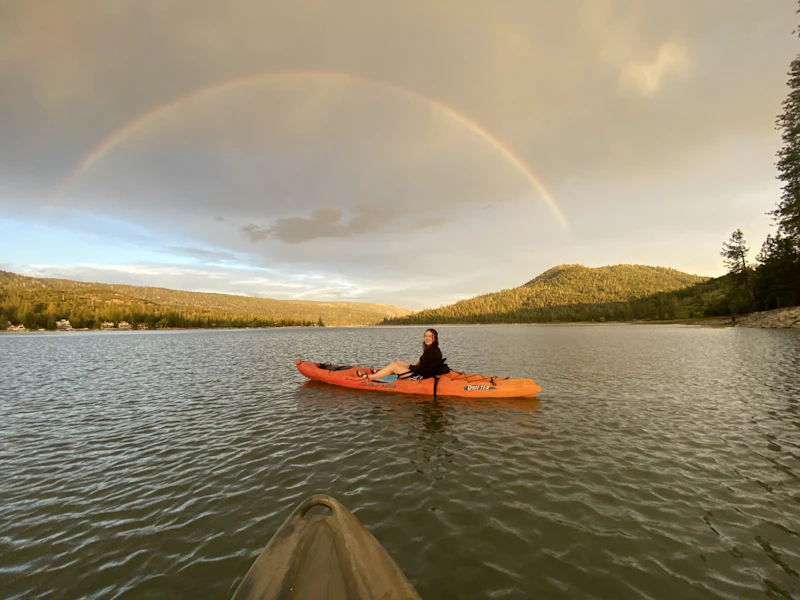 a woman in an orange kayak in a small lake beneath a rainbow