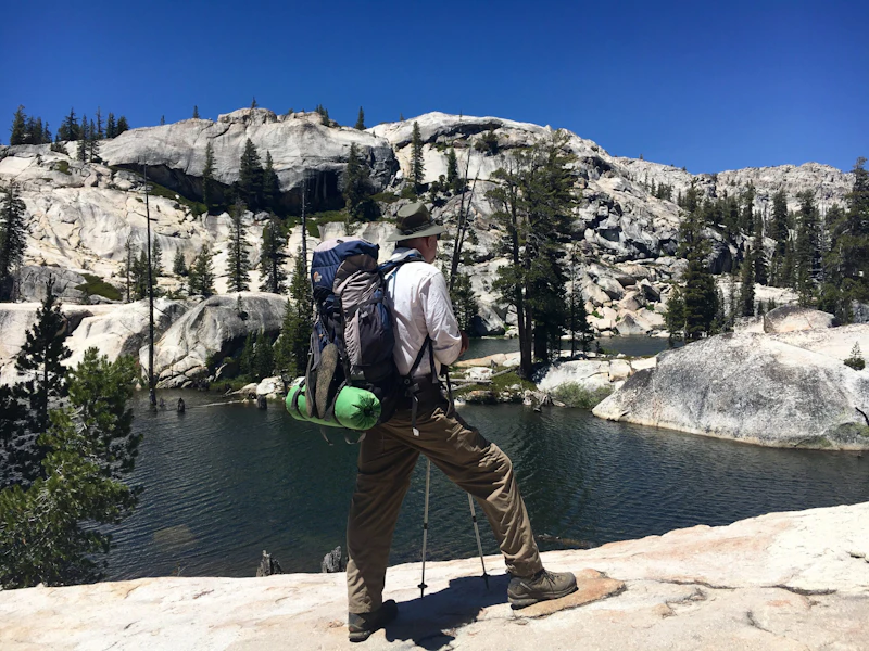 backcountry hiker stands at the edge of an alpine lake