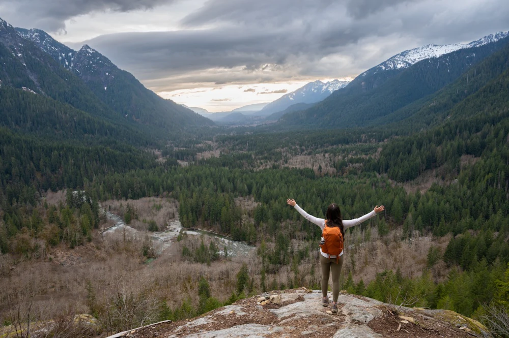 a woman with arms outstretched in front of a mountain valley