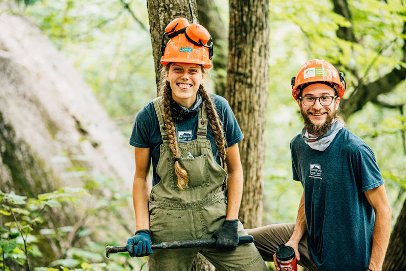 a young man and woman in hard hats working in the forest.