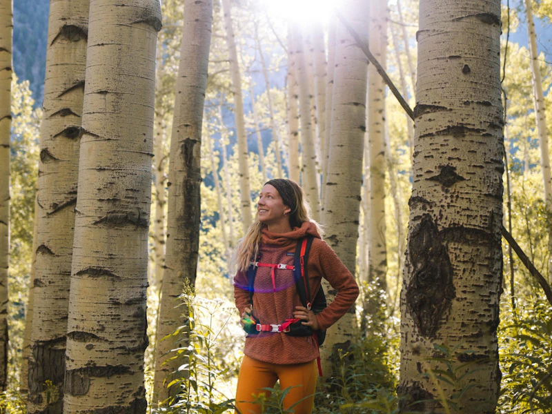 a woman with a backpack stands in sunshine and aspens